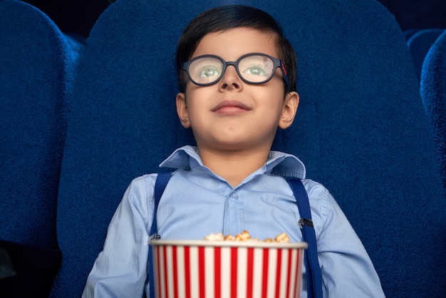 Niño con cubo de palomitas de maíz viendo dibujos animados en el cine.