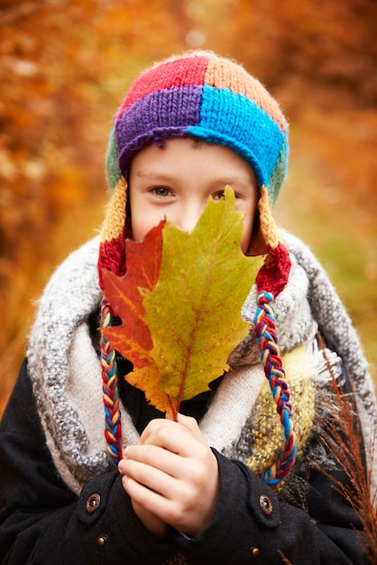 Niño cubriendo la cara con hojas de otoño