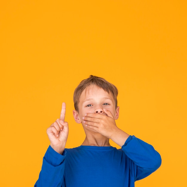 Foto gratuita niño cubriendo su boca y apuntando hacia arriba