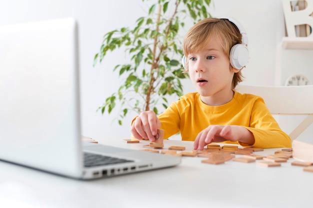 Niño curioso usando laptop y auriculares en casa