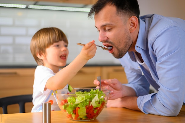 Niño dando a su padre ensalada para comer