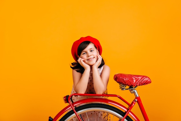 Foto gratuita niño despreocupado en boina francesa posando con bicicleta foto de estudio de niña preadolescente caucásica aislada en amarillo