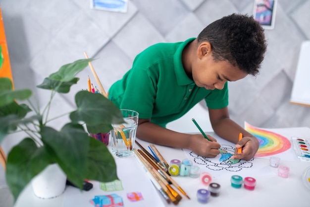 Niño dibujando con lápiz de color de pie en la mesa