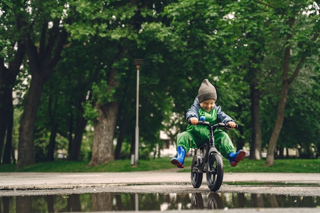 Niño divertido en botas de lluvia jugando en un parque de lluvia