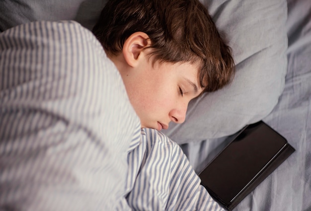 Foto gratuita niño dormido con móvil al lado