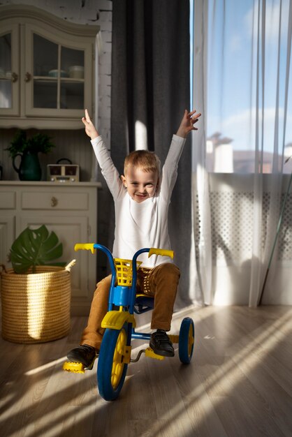 Niño emocionado de tiro completo en triciclo en el interior