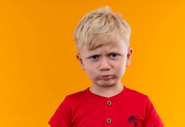 Foto gratuita un niño enojado con cabello rubio y ojos azules con camiseta roja mirando