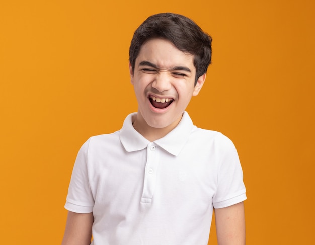 Niño enojado gritando con los ojos cerrados aislado en la pared naranja