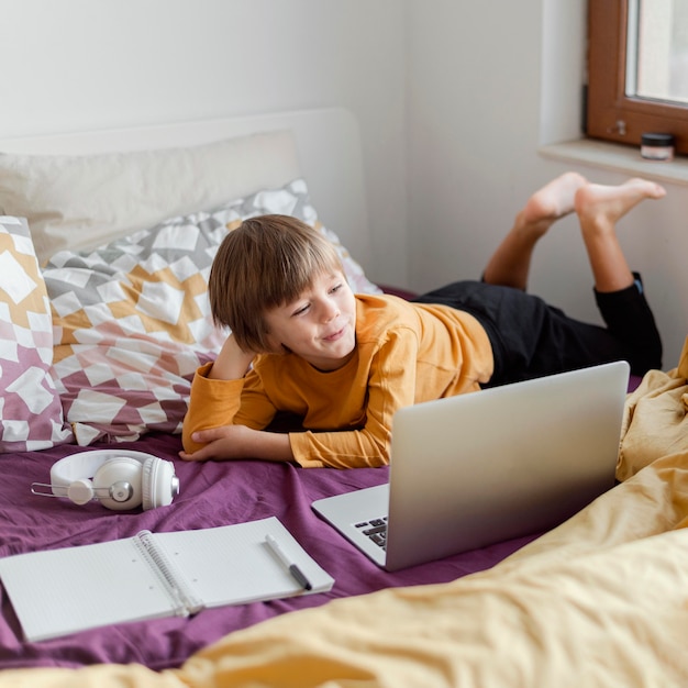 Niño de escuela sentado en la cama con su computadora portátil