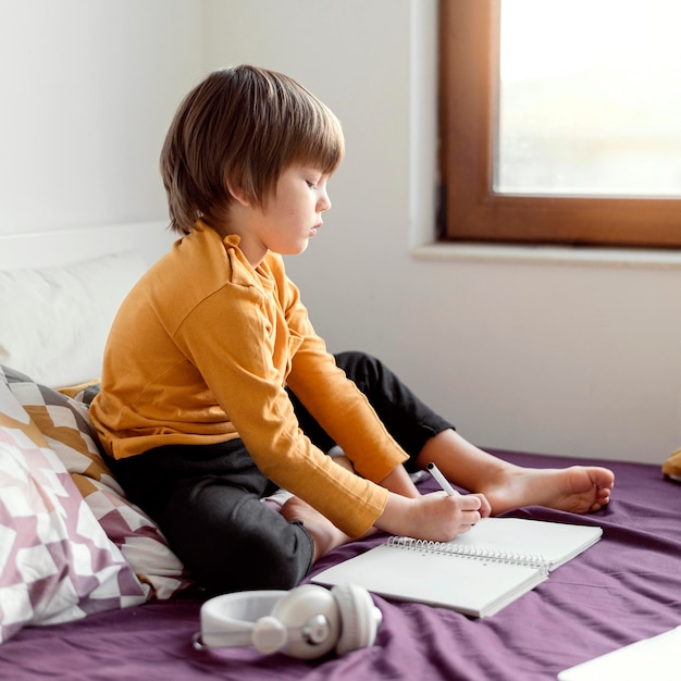 Foto gratuita niño de escuela sentado en la cama vista lateral