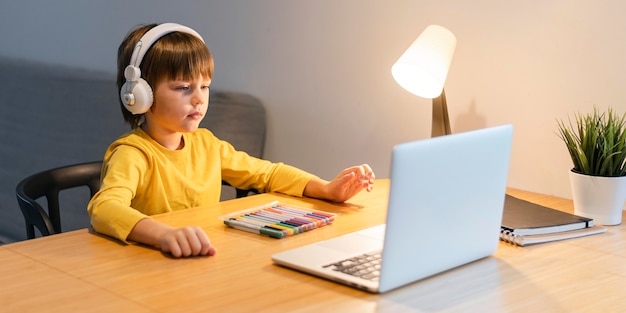 Foto gratuita niño de escuela de vista lateral en camisa amarilla tomando clases virtuales