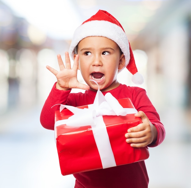 Niño expresivo sujetando un regalo con un lazo blanco