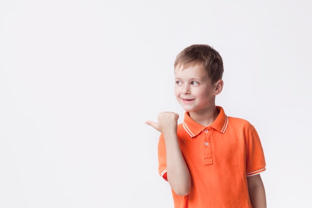 Niño feliz apuntando al lado con el pulgar sobre fondo blanco