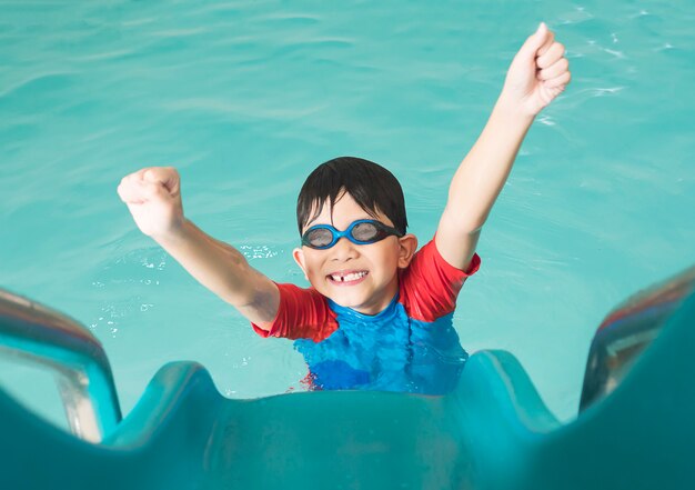 Niño feliz asiático que juega el resbalador en piscina