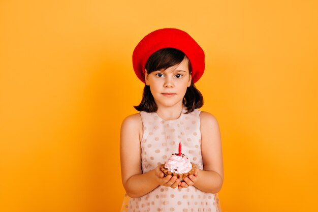 Niño feliz en boina francesa celebrando cumpleaños. niña preadolescente extasiada con pastel aislado en la pared amarilla.