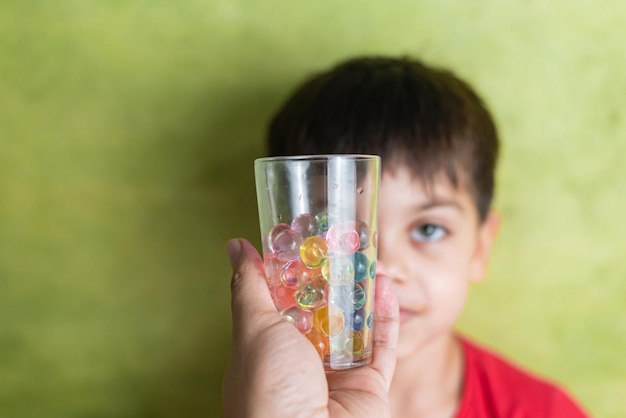 Foto gratuita niño feliz en camiseta roja con taza de bolas orbeez