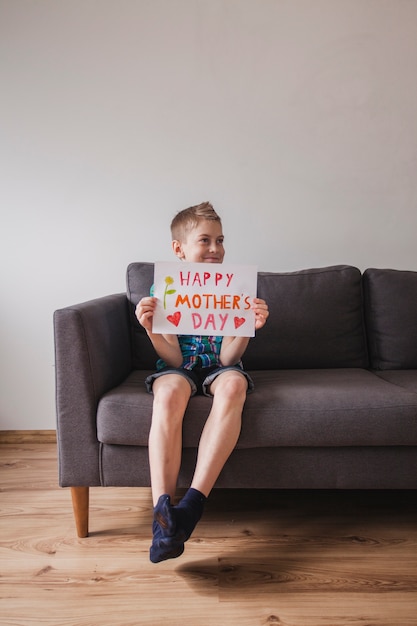 Niño feliz con cartel del día de la madre sentado en un sillón