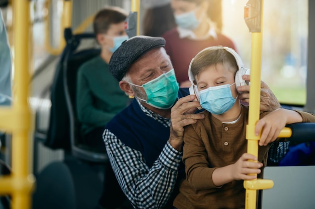 Niño feliz disfrutando de la música con auriculares mientras viaja en autobús con su abuelo