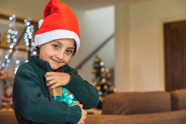 Niño feliz en gorro navideño con caja actual