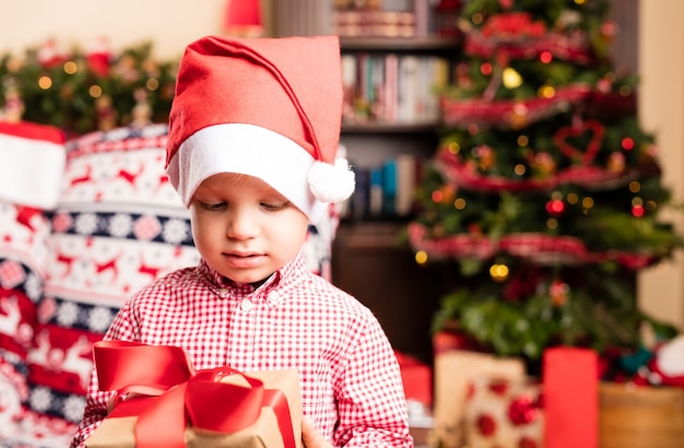 Niño feliz con gorro de papá noel sujetando un regalo