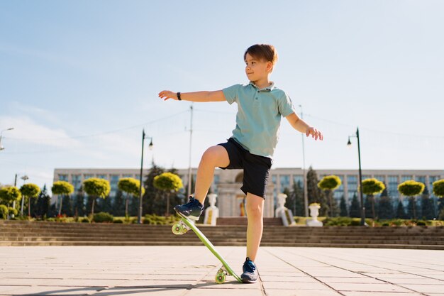 Niño feliz jugando en patineta en el parque, niño caucásico montando penny board, practicando patineta.