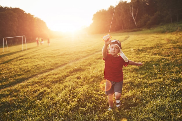 Niño feliz lanzar una cometa en el campo al atardecer. Pequeño niño y niña en vacaciones de verano