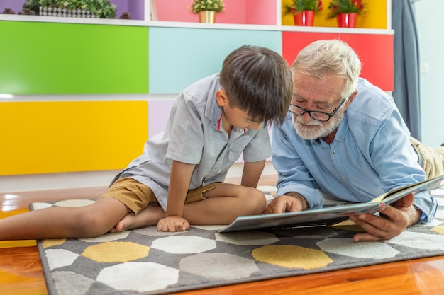 Niño feliz nieto leyendo un libro con el anciano abuelo en casa