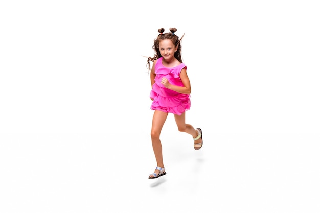 Niño feliz, niña caucásica pequeña y emocional saltando y corriendo aislado en blanco