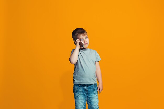 El niño feliz de pie y sonriendo contra la pared naranja