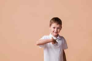Foto gratuita niño feliz señalando con el dedo a sí mismo de pie cerca de la pared de color beige
