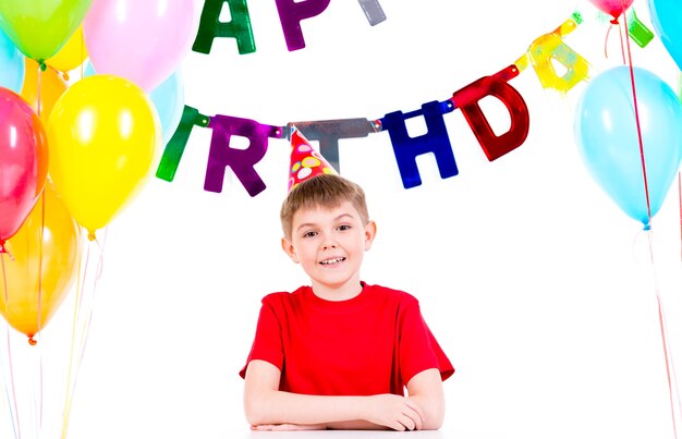 Niño feliz sentado en la mesa divirtiéndose en una fiesta de cumpleaños - aislado en un blanco.