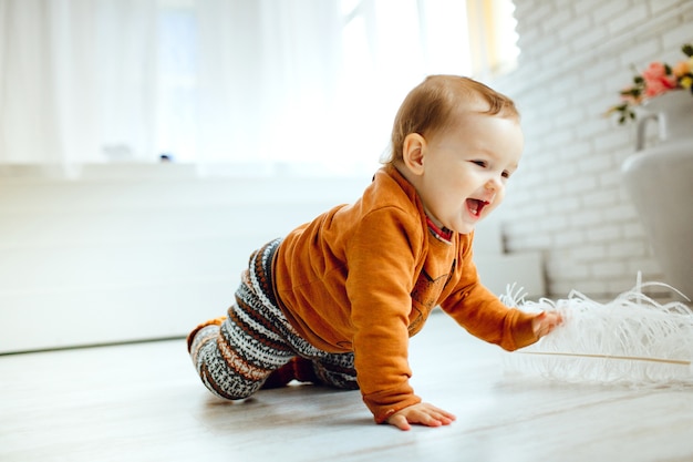 Niño feliz en suéter naranja juega con plumas en el piso
