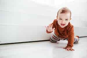 Foto gratuita niño feliz en suéter naranja juega con plumas en el piso