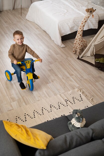 Niño feliz de tiro completo sentado en triciclo de ángulo alto