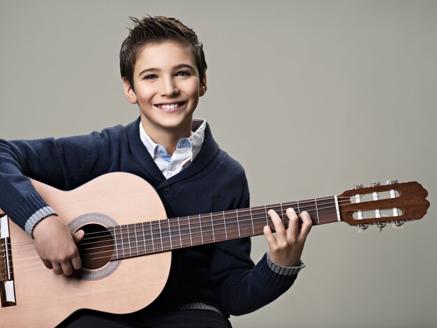 Niño feliz tocando la guitarra acústica.