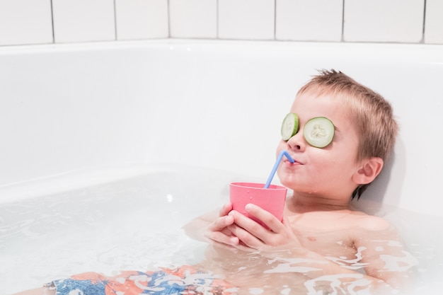 Niño feliz tomando un baño relajante en una bañera de hidromasaje, bebiendo jugo