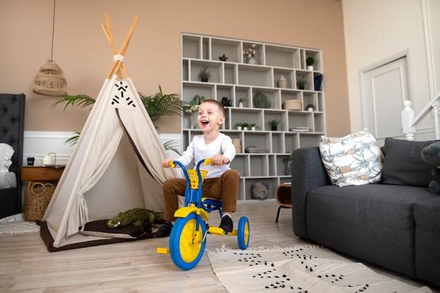 Foto gratuita niño feliz con triciclo en el interior tiro completo