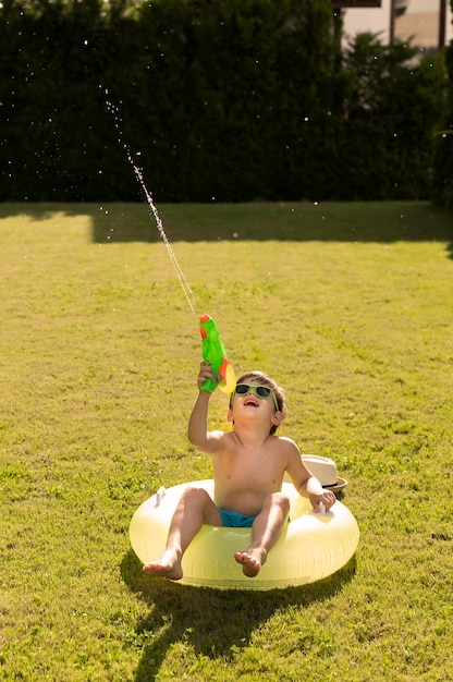 Foto gratuita niño en flotador jugando con pistola de agua