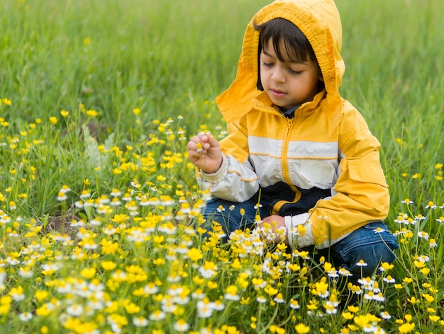 Niño en gabardina recogiendo flores