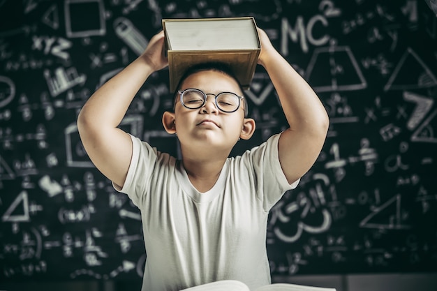 Foto gratuita un niño con gafas estudió y se puso un libro en la cabeza en el aula.