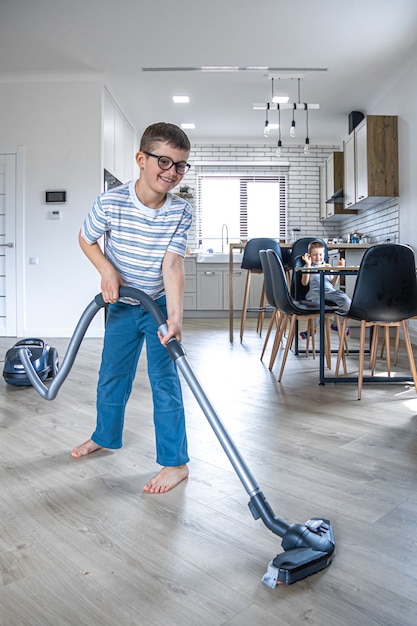 Un niño con gafas limpia la casa con una aspiradora.