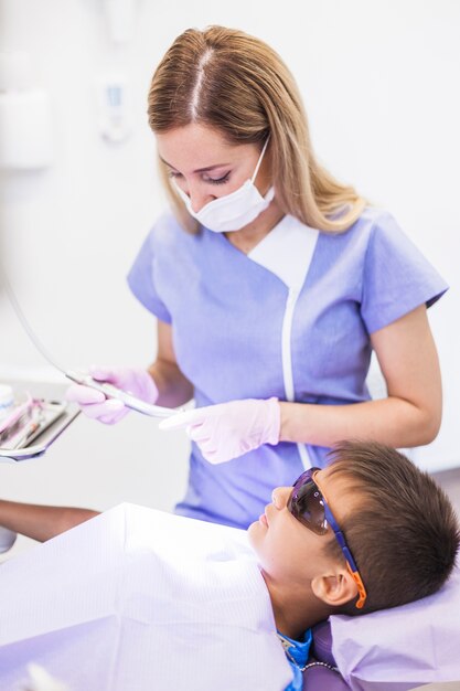 Niño con gafas protectoras de seguridad apoyadas en una silla dental frente a un dentista