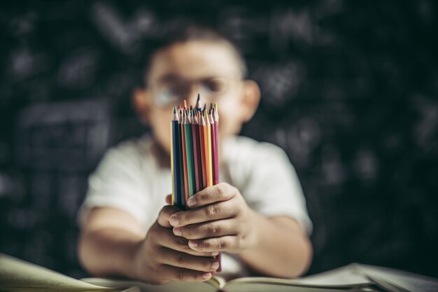 Un niño con gafas sentado con muchos lápices de colores.