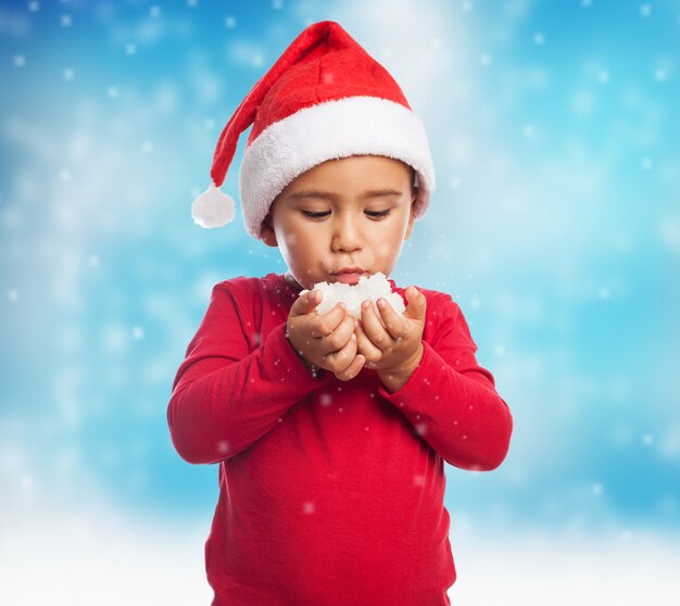 Niño con gorro de santa y soplando la nieve de sus manos