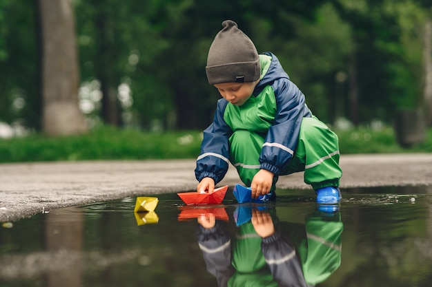 Niño gracioso en botas de lluvia jugando en un parque de lluvia