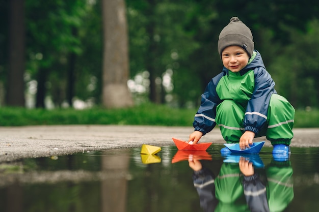 Niño gracioso en botas de lluvia jugando en un parque de lluvia