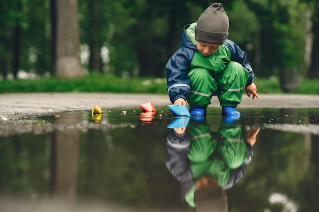 Niño gracioso en botas de lluvia jugando en un parque de lluvia