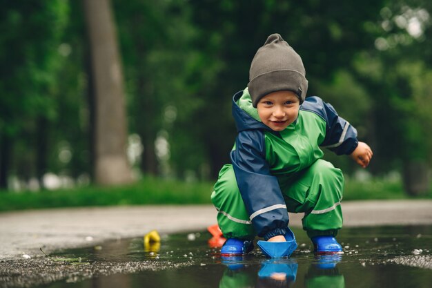 Niño gracioso en botas de lluvia jugando en un parque de lluvia