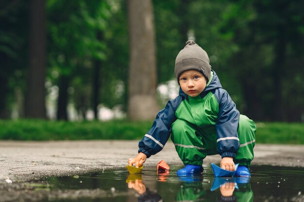 Niño gracioso en botas de lluvia jugando en un parque de lluvia