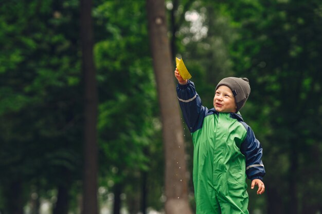 Niño gracioso en botas de lluvia jugando en un parque de lluvia